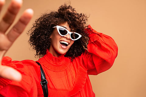 Retrato de una hermosa joven mujer negra tomándose selfie. Retrato de una bonita joven mujer afroamericana con ropa de estilo retro sonriendo mientras está de pie y tomándose una selfie aislada sobre beige.