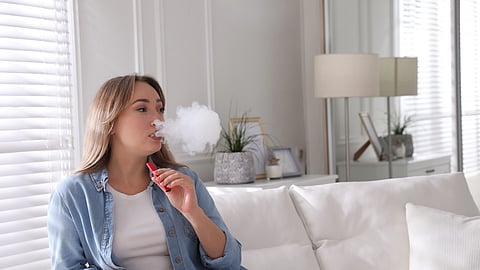 Hermosa mujer joven usando cigarrillo electrónico desechable en el sofá de casa