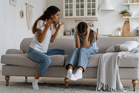 Madre enojada y loca tratando de disciplinar al niño, expresando frustración gritando a la hija adolescente sentada en el sofá tapándose los oídos con las manos. Efectos psicológicos de gritarles a los niños, abuso verbal
