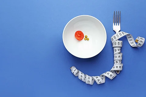 Plato con verduras, tenedor y cinta métrica sobre fondo de color. Concepto de anorexia