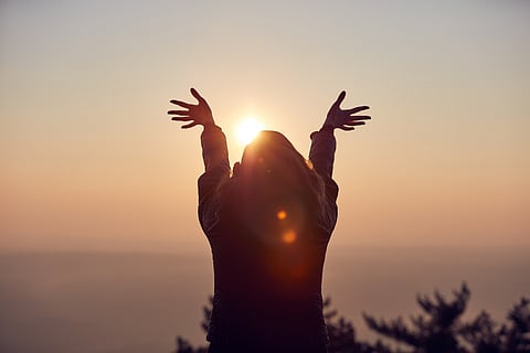 Mujer con los brazos abiertos disfrutando de la hora de salida / puesta del sol.