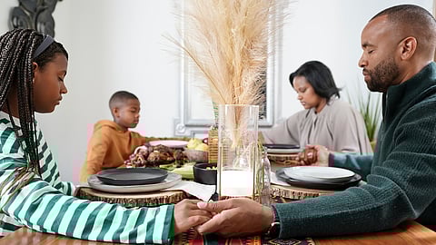 Familia con niños (8-9, 12-13) rezando antes de la comida de Kwanzaa