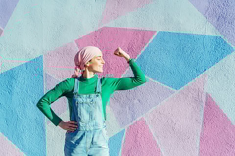 Retrato de mujer con pañuelo rosa en la cabeza, tiene cáncer. Muestra el brazo como señal de fuerza