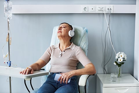 Retrato de una mujer mayor usando relajación con auriculares durante tratamiento de goteo intravenoso en el hospital