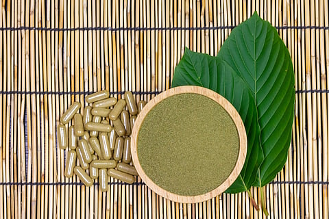 Mitragyna Speciosa Korth o polvo de kratom en un cuenco de madera con cápsulas y hoja verde sobre esterilla de madera, vista superior y espacio para copiar.