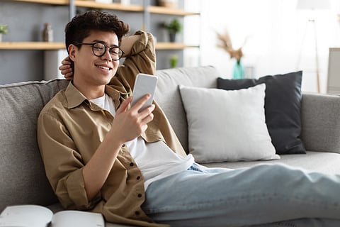 Hombre asiático sonriente con gafas usando smartphone en casa