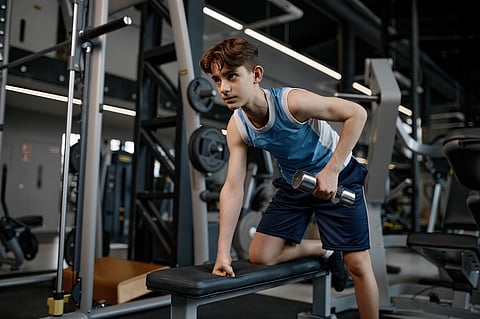 Chico adolescente concentrado entrenando brazos y hombros con mancuernas