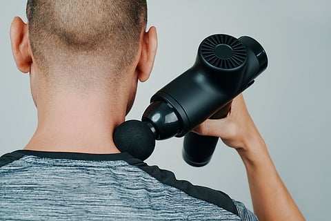 deportista usando una pistola de masaje en el cuello