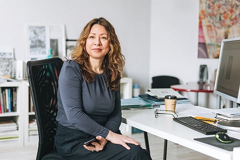Mujer adulta encantadora, sonriente y de mediana edad con pelo rizado, diseñadora y gerente trabajando en una oficina moderna y luminosa