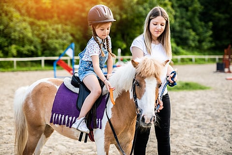 Niña pequeña y su hermana mayor disfrutando con un pony al aire libre en un rancho.