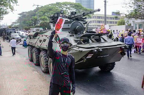 A protester holds a placard with the three-finger salute in front of a military tank in front of the Central Bank building during a demonstration. February 2021, Yangon, Myanmar. Photo: IMAGO / ZUMA Wire.