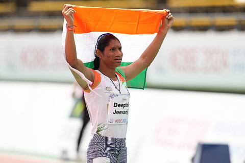 Deepthi Jeevanji, an Indian para-athlete with long black hair pulled back holds the Indian flag high with both her hands