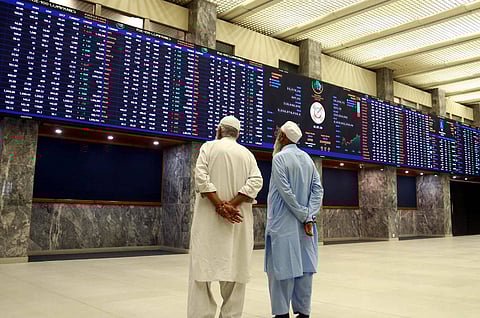 Two men dressed in salwar kurta with their hands behind their backs looking up at trading screens at the Pakistan stock exchange in Karachi