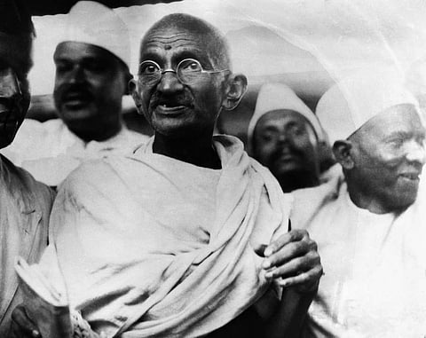 Black and white photo of Mohandas Karamchad Gandhi with four other men in the background.