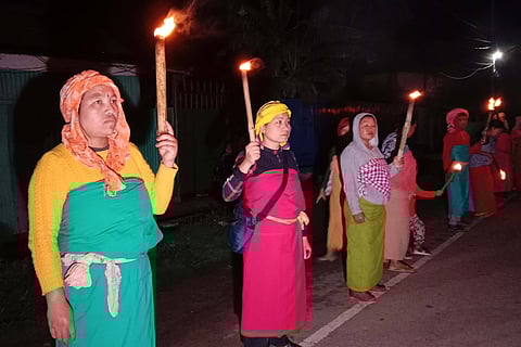Women dressed in traditional attire stand in line holding lit torches on a late evening in Manipur in June 2023