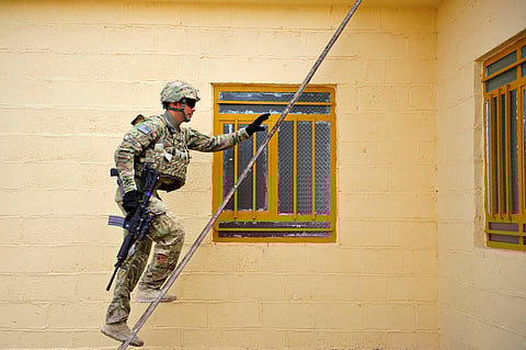 A man in US military uniform carrying a gun climbing a ladder.