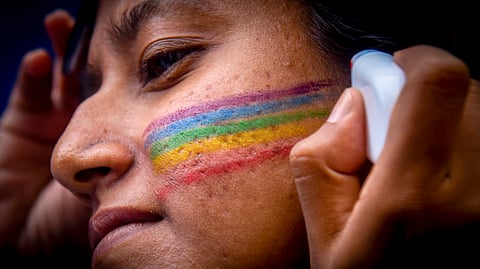 A close up of a person's face, and of someone else's hands drawing on the pride colours with a special pen. This is a photo from the 2024 Pride Parade in June in Colombo, where the queer community marched calling for decriminalisation of same sex relationships, but also highlighted labour rights, gender issues, and chanted in solidarity with Palestine.