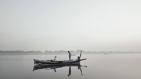 Two men on a boat floating on a still lake. Photo is in grey scale. This is a photo from Indus Echoes, a film shot in Sindh, Pakistan.