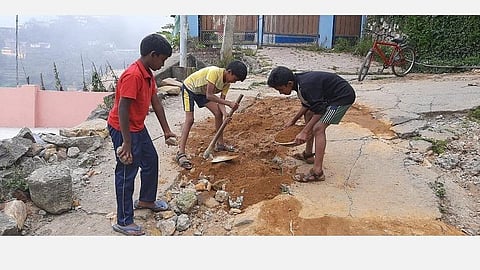 கொடைக்கானல் ஆனந்தகிரி பகுதியில் சேதமடைந்த சாலையை சீரமைக்கும் பள்ளி மாணவர்கள்.