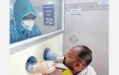 திண்டுக்கல் அரசு மருத்துவமனையில் கண்ணாடி கூண்டுக்குள் இருப்பவரிடம் இருந்து சளி மாதிரியை சேகரிக்கும் மருத்துவர்.