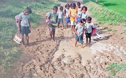 சிவகங்கை அருகே மாரந்தை கிராமத்தில் சேறும், சகதியுமான சாலையில் சிரமப்பட்டு நடந்துசெல்லும் பள்ளிக் குழந்தைகள்.