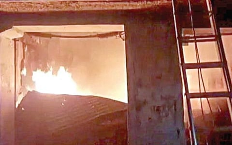 மரக்கிடங்கில் தீயில் இறந்த ஒருவரின் சடலத்தை வெளியே கொண்டு வரும் தீயணைப்பு வீரர்கள். (அடுத்த படம்) மரக்கிடங்கில் உட்புறம் யாரும் செல்ல முடியாதபடி கொழுந்துவிட்டு எரிந்த தீ.