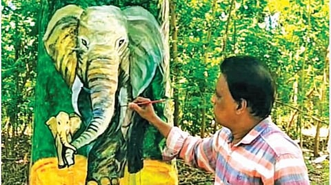 மரங்களில் விழிப்புணர்வு ஓவியங்களை வரையும் அரசு பள்ளி நுண்கலை ஆசிரியர் அன்பு.