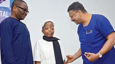 சிகிச்சைக்கு பிறகு இயல்பு நிலைக்கு திரும்பிய நைஜீரியாசிறுமி பேட்ரிசியாவுடன் மருத்துவர் எம்.எஸ்.பாலாஜி. உடன் சிறுமியின் தந்தை பேட்ரிக். | படம்: பு.க.பிரவீன் |