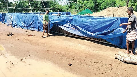 ஈரசெங்கல்லை தார்படுதாவைக் கொண்டு மூடும் பணியில் தொழிலாளர்கள். | இடம்: உடையாளூர்.