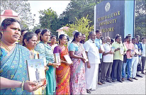 வேலூர் திருவள்ளுவர் பல்கலை. நுழைவுவாயில் முன்பாக `திருவள்ளுவர் பல்கலைக்கழகத்தில் தில்லுமுல்லு' என்ற புத்தகத்துடன் பல்கலை. தொழிலாளர் சங்கத்தினர். படம்: வி.எம்.மணிநாதன்