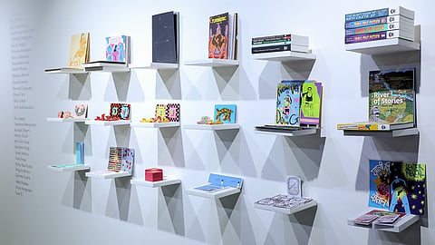 A gallery wall with small white floating shelves displaying independent art books, zines, and small objects at Pulp Bazaar.