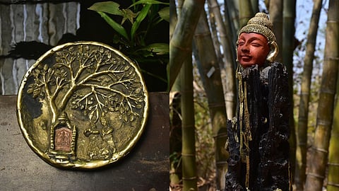 A brass plate with a tree motif next to a Buddha head on dark wood.