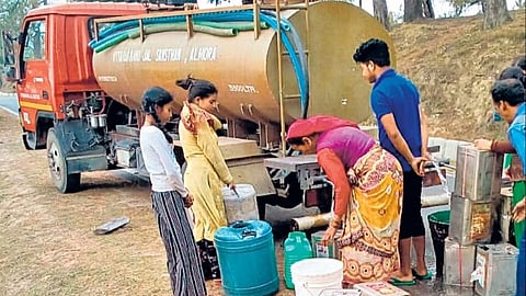 अल्मोड़ा के डिनापानी गांव के ग्रामीण टैंक से पानी लेते हुए