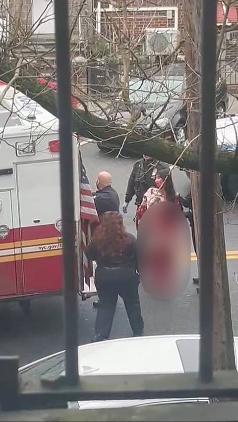 One of the blood-soaked victims stands in distress as emergency responders attend to the scene in Bensonhurst, Brooklyn.