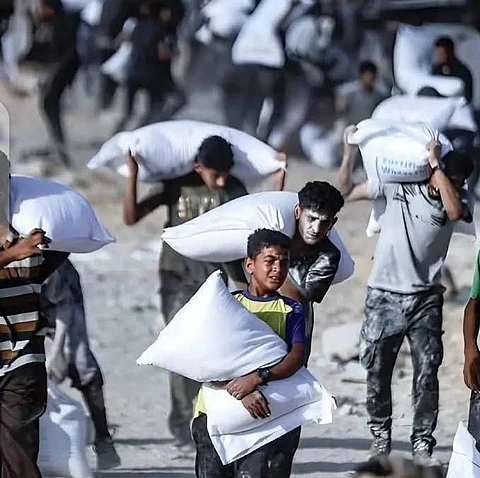 Starving Palestinians, including children, carrying bags of flour.
