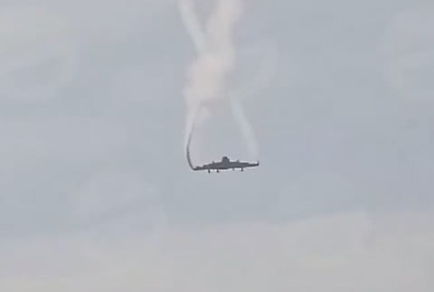 A close-up view of a Turkish Air Force C-130 military transport plane in mid-air, trailing a thick plume of white smoke.