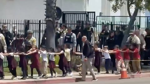 Police and armed officers tactically escorting a long chain of young children holding hands out of the Islamic Center of San Diego mosque complex the incident.