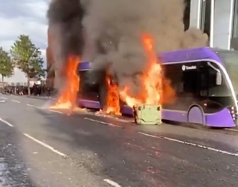 A public bus ablaze amid street unrest in Belfast, capturing thick black smoke and flames from a vehicle set on fire during protests.
