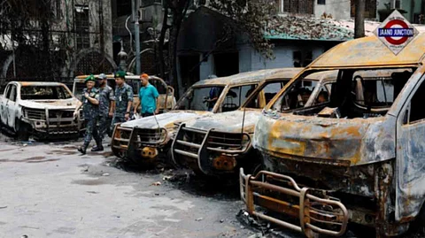 Security personnel walk past damaged vehicles of a government owned organization, that were set afire by a mob during clashes after violence erupted following protests by students against government job quotas, in Dhaka, Bangladesh, July 22, 2024.