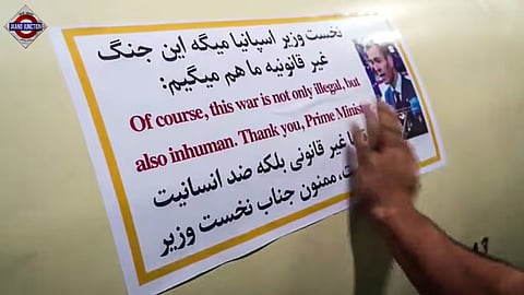 An IRGC fighter affixes a sticker bearing Spanish PM Pedro Sanchez’s image and an anti-war quote attributed to him.