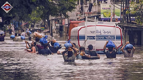 People carry packets of food items on their heads as they wade through a waterlogged road after heavy rain, in Surat.