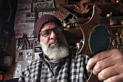 Reflections of Tradition: Mohammad Aslam Bhat gazes at his reflection in a handcrafted copper-framed mirror inside his 'Van Posh' workshop in Srinagar, Kashmir.