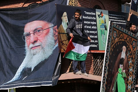 A young protester climbs the Lal Chowk Clock Tower in Srinagar and drapes posters of Ayatollah Ali Khamenei while holding a Palestinian flag during the protest.