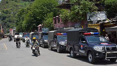 Commuters ride past security personnel as they patrol a street ahead of a protest by the Joint Awami Action Committee (JAAC) in Muzaffarabad, Pakistan administered Jammu and Kashmir.