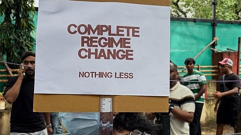 A poster carried by a protester at Jantar Mantar calls for "Complete Regime Change, Nothing less" in Delhi during Cockroach Janta Party sit-in in July 2026.