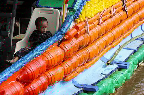 صبي يجلس على متن قارب مصنوع من مواد معاد تدويرها في جاكرتا، إندونيسيا.