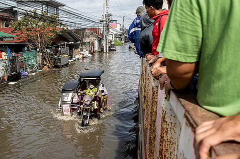 أشخاص يركبون دراجة نارية مع عربة جانبية أثناء عبورهم طريقًا غمرته المياه بعد الفيضانات التي تسبب بها المد العالي والإعصار الفائق فونغ-وونغ، في بلدة ماكابيبي، مقاطعة بامبانغا، الفلبين، 10 نوفمبر 2025.
