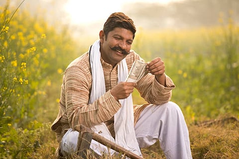 Portrait of happy farmer holding Indian Rupee notes in rapeseed agricultural field