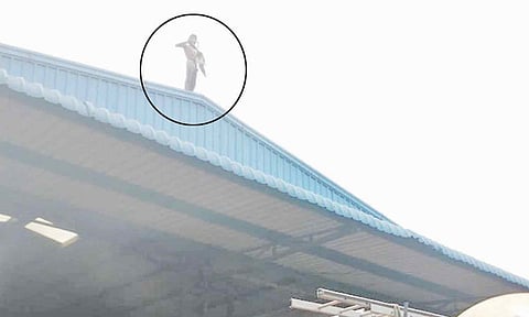 தொழிற்சாலையின் மேற்கூரையில் ஏறி நிற்கும் வடமாநில வாலிபர்.