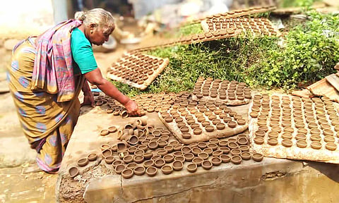 அகல்விளக்குகளை காய வைக்கும் பணியில் ஈடுபட்டுள்ள பெண்.